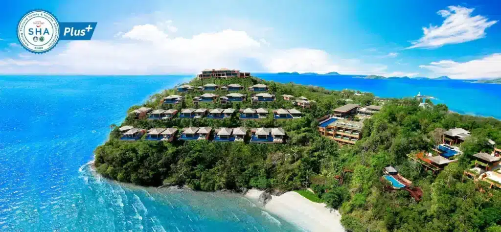 A lush, green hillside Phuket resort overlooking the ocean with multiple bungalows and villas spread across the landscape. The blue sea surrounds the hill, and the sky is clear with a few white clouds. Recommended among top hotels in Phuket, it features a "SHA Plus+" badge for safety and health certification.