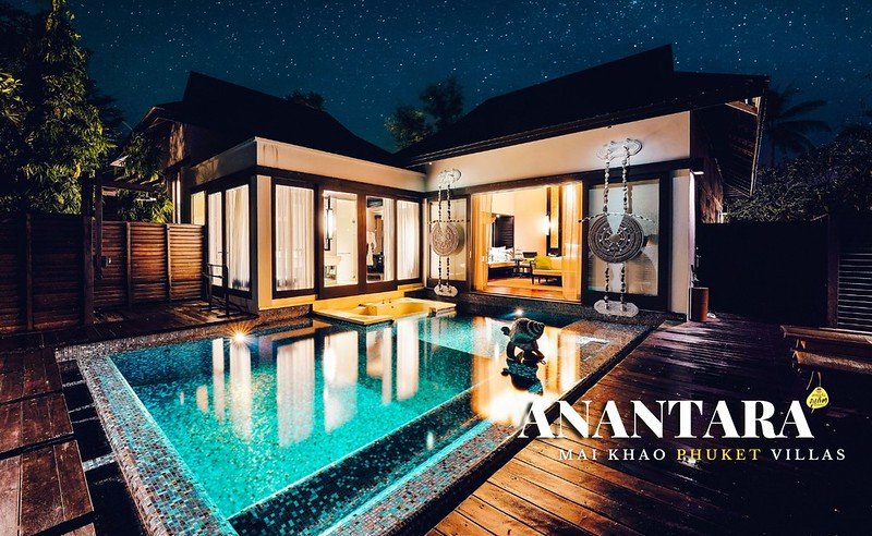 A luxurious villa with a modern design, illuminated at night. It features large glass doors and windows opening to a private pool. Wooden deck surrounds the pool, and decorative elements adorn the Phuket pool villa. The text "ANANTARA MAI KHAO PHUKET VILLAS" is displayed at the bottom right.