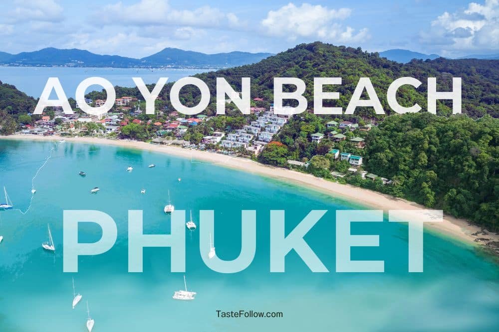 Aerial view of Ao Yon Beach in Phuket, Thailand. The tranquil bay features turquoise waters with several boats anchored near the shore. The beach, one of the underrated beaches in Phuket, is lined with lush greenery and backed by a hillside dotted with buildings. Text overlay reads "AO YON BEACH PHUKET.