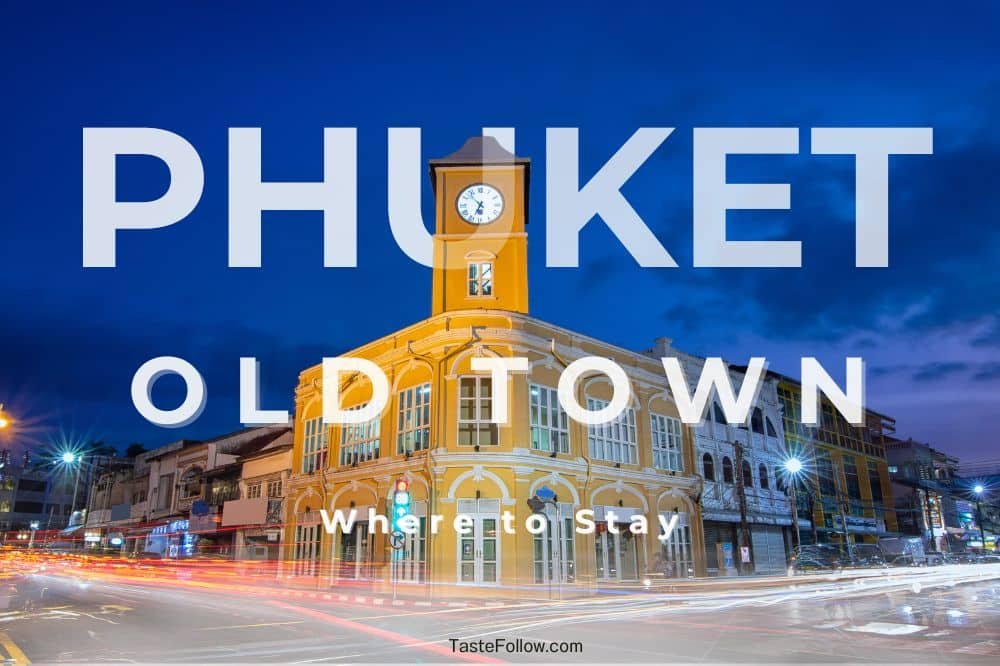 An illuminated yellow clock tower stands prominently in Phuket Old Town during twilight. Long exposure light trails from passing cars streak across the street, creating a dynamic effect. Bold text reading "PHUKET OLD TOWN" and "Best Places to Stay in Phuket Town" overlays the image. The sky is deep blue.