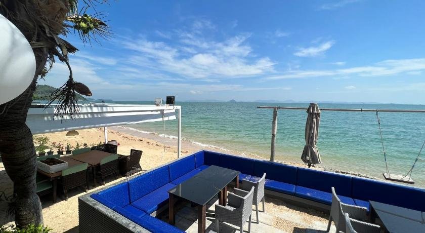 An inviting outdoor seaside dining area with a blue cushioned corner seating arrangement and several gray chairs around black tables, this spot overlooks the tranquil sea under a clear blue sky. Located at one of the luxury beachfront resorts in Phuket, it features festive balloon decorations and white structures on a sandy beach.