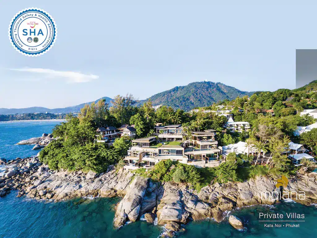 Aerial view of a coastal resort in Kata Noi, Phuket, featuring luxury beachfront resorts with multiple private villas nestled among trees on rocky terrain beside the ocean. The sky is clear, revealing nearby hills. The image includes logos for SHA Thailand and Impiana Private Villas in the top left and bottom right corners, respectively.