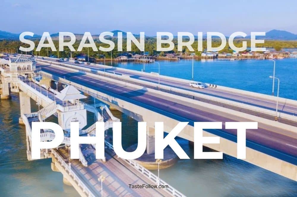 Aerial view of the Sarasin Love Bridge connecting Phuket Island to mainland Thailand. The bridge spans blue waters with a few boats visible. The area features surrounding greenery and mountains in the background. Large white text labeled "SARASIN BRIDGE PHUKET" overlays the image.